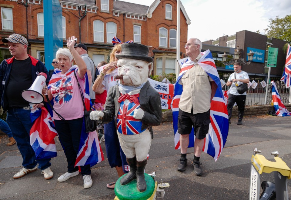 Protestors with Union Jack flags and a John Bull statue outside a Manchester hotel.