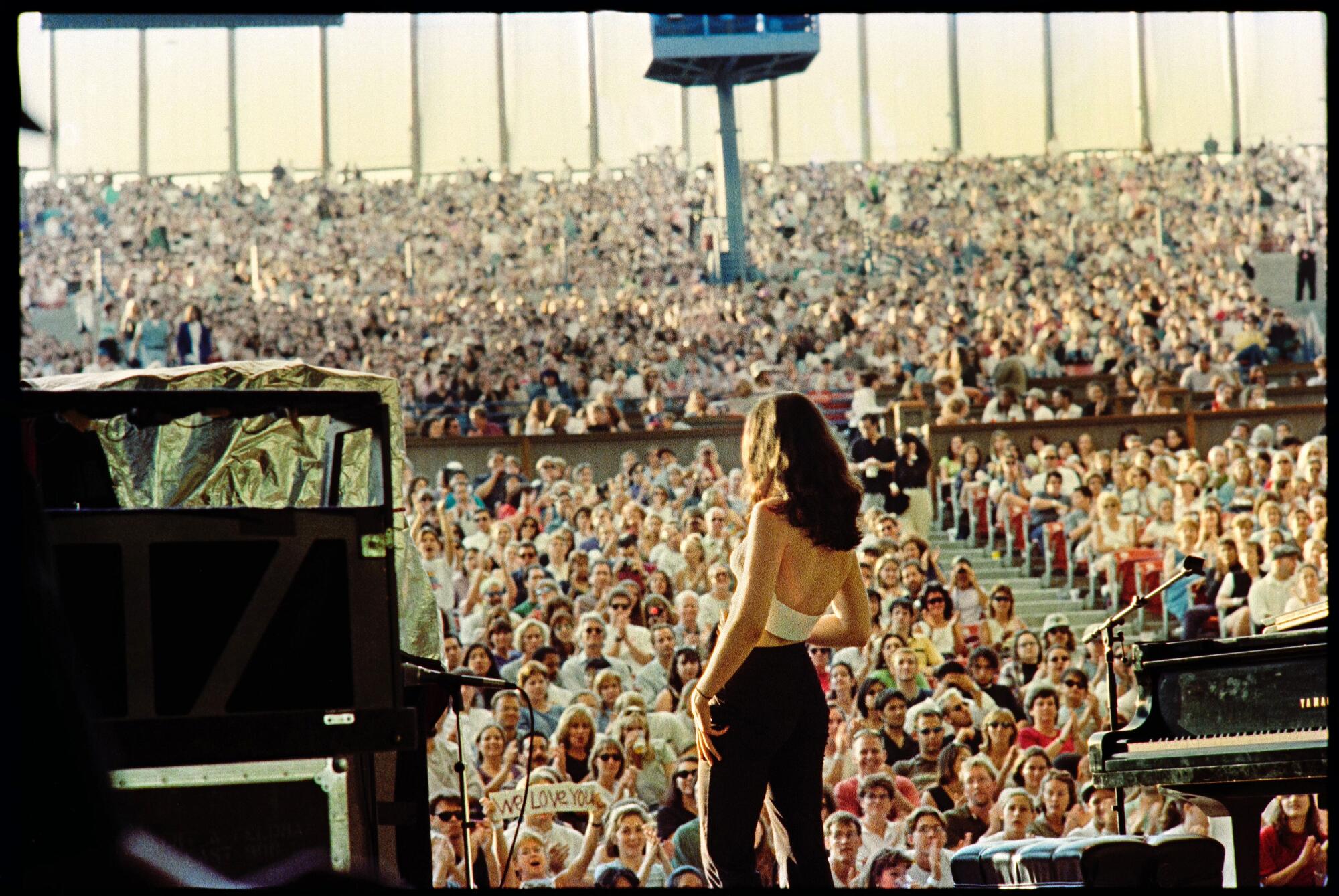 A woman, seen from the back, standing on stage in front of a large crowd in a stadium.