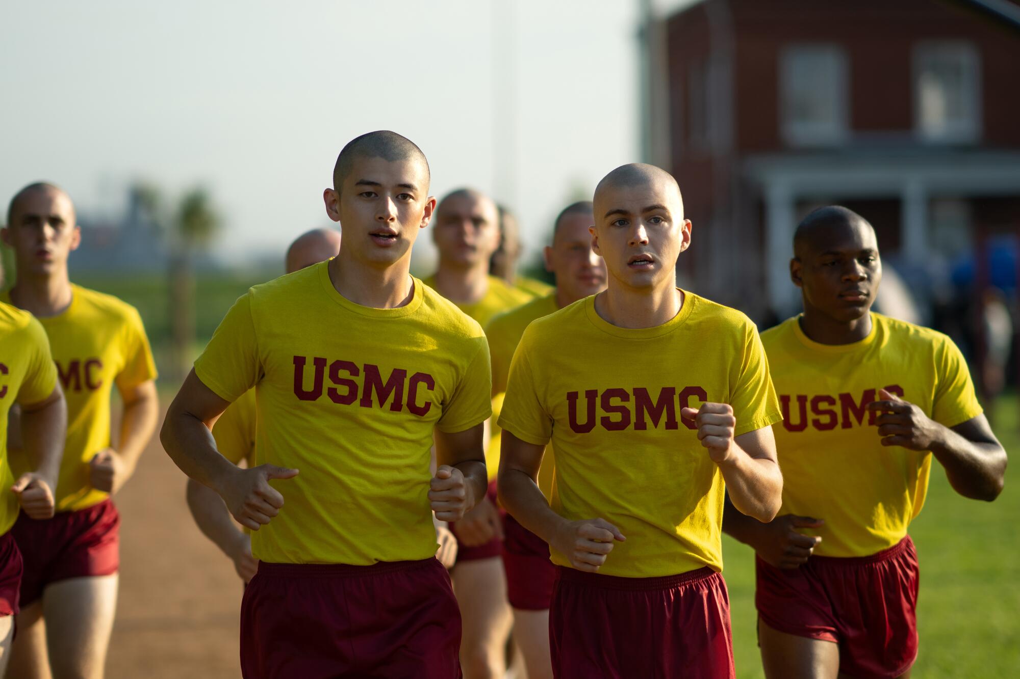 A group of men in yellow T-shirts with USMC in red across them and red shorts jog on a path.