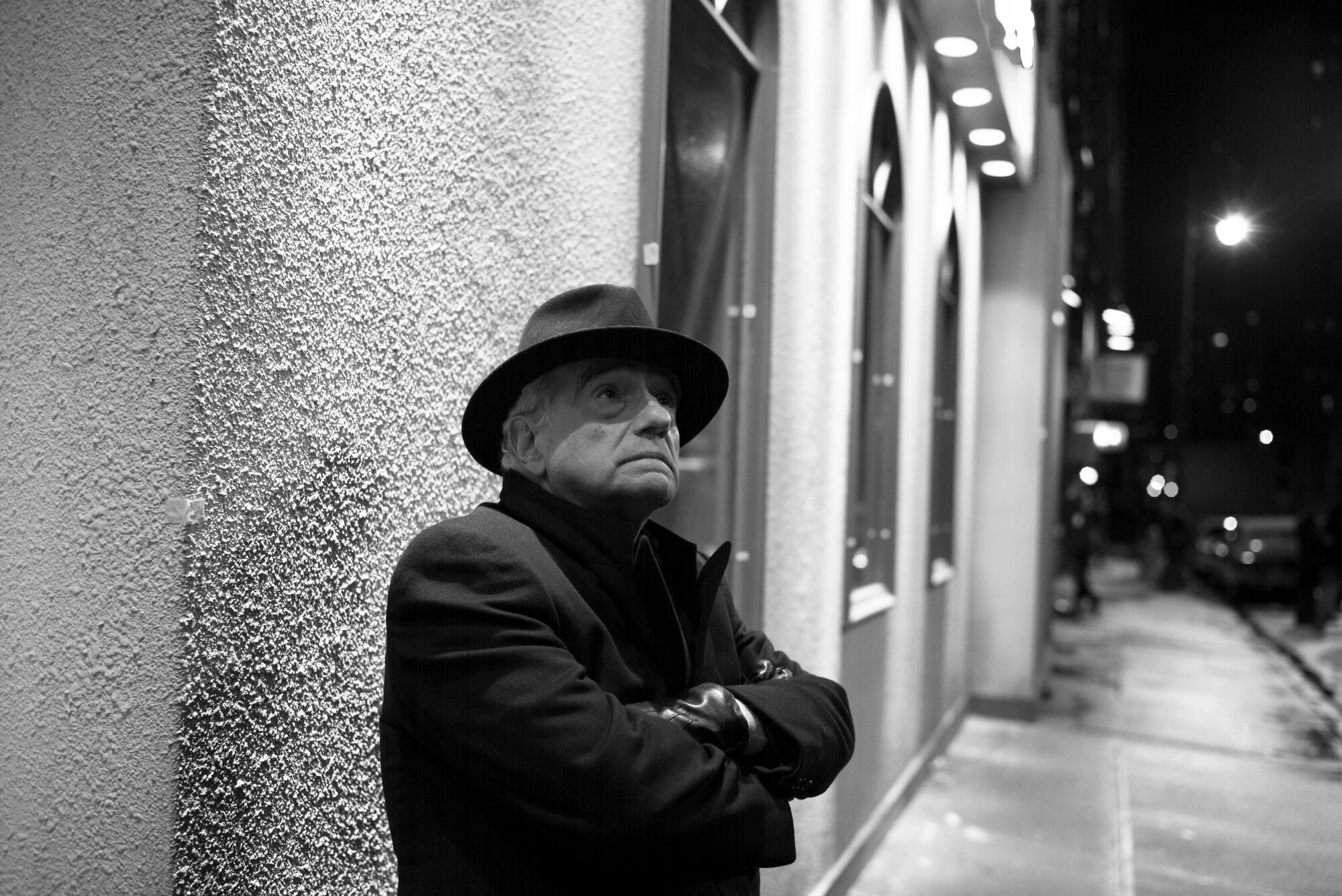 A man in a hat and coat standing near a building wall.