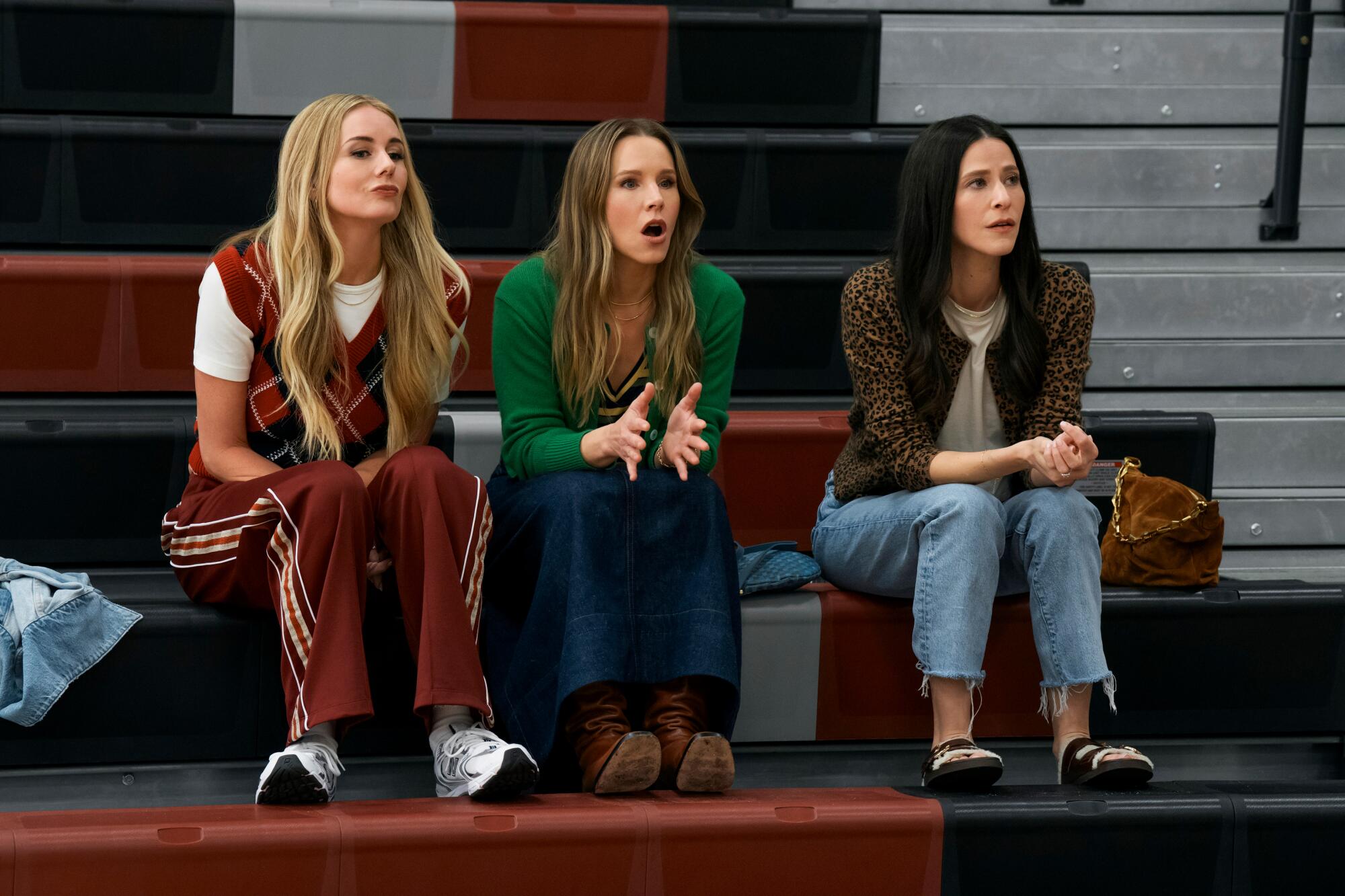Three women sitting on bleachers in a gymnasium.