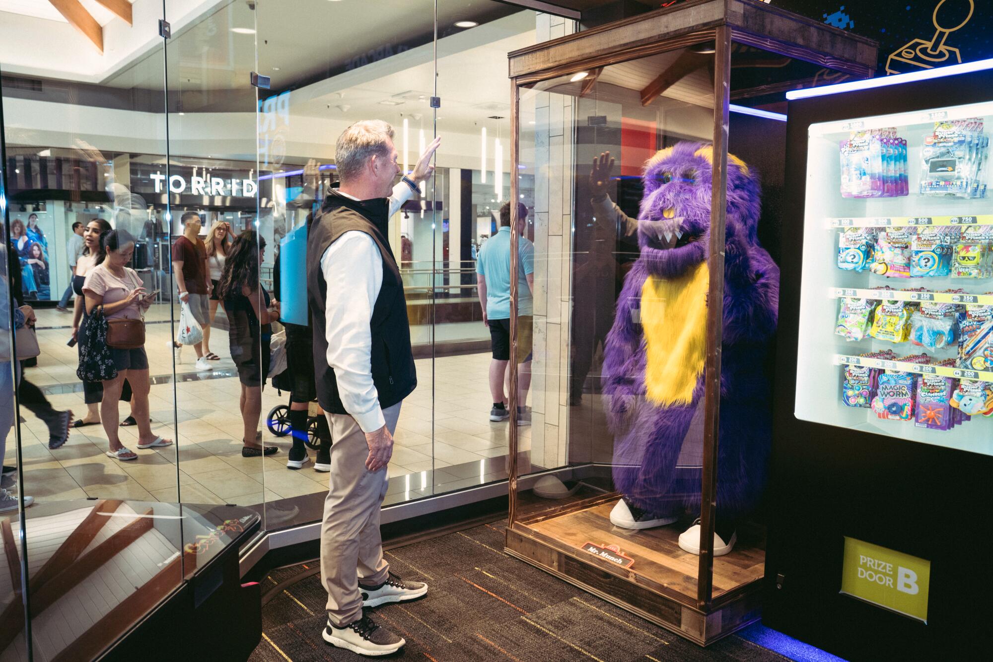 A man in a vest jacket in front of a purple animatronic.