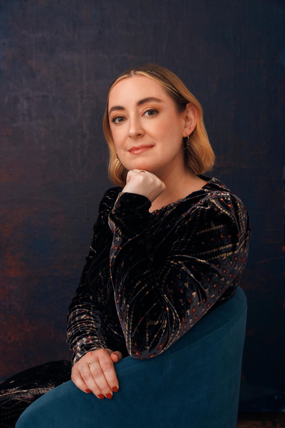 Leigh Stein sits on a dark turquoise chair and rests her fist under her chin.