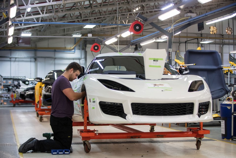 Worker assembling a white Lotus Evora sports car on a production line.