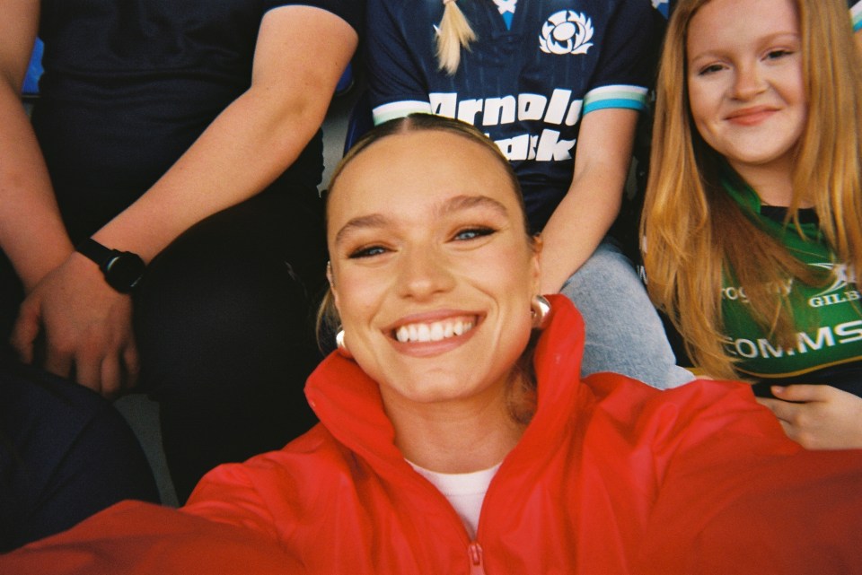 Selfie of a woman smiling, surrounded by people wearing sports jerseys.