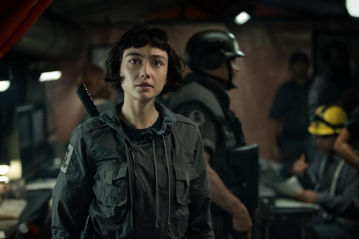 A woman with a bob hairstyle stands in a combat uniform