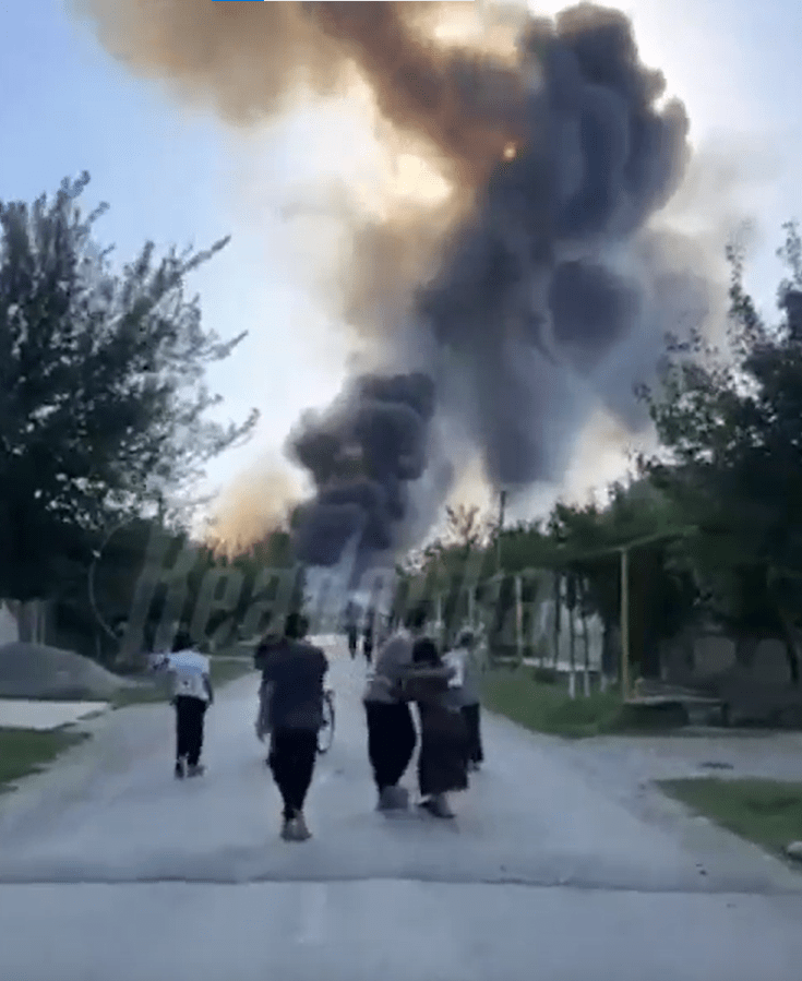 People evacuating as a large fire burns in the distance.