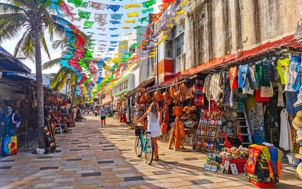 Playa del Carmen street scene with shops, pedestrians, and colorful banners.