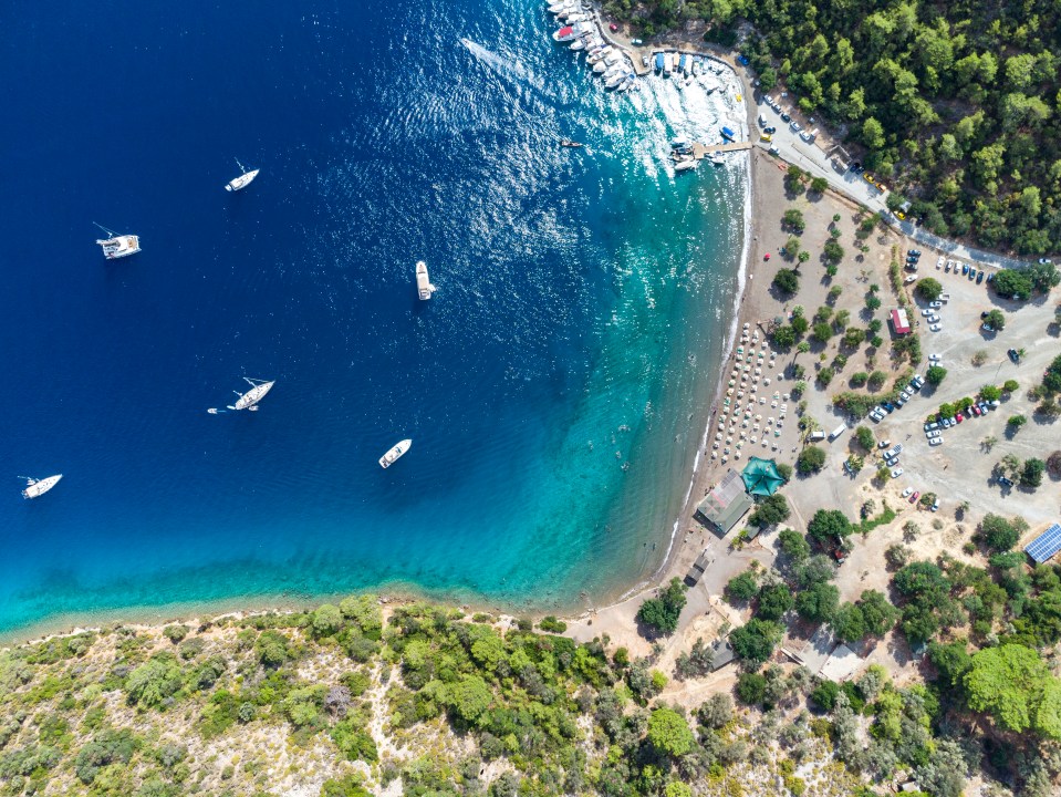 Aerial view of Sarsala Bay, Mugla Dalaman, showing boats in the water and a beach with people.