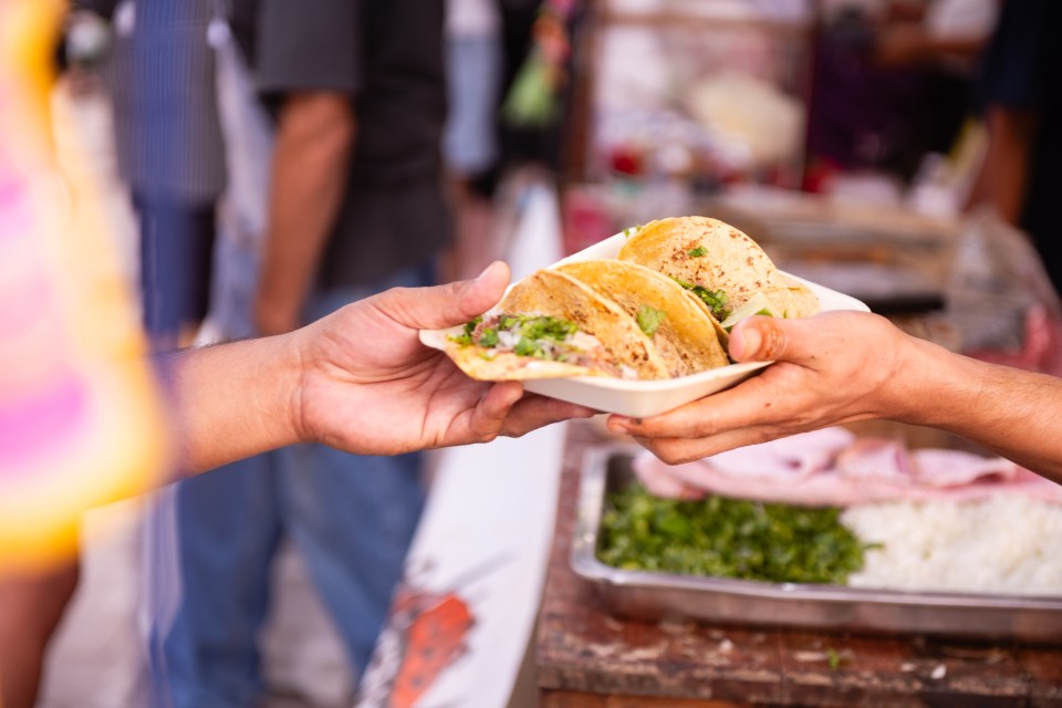 Tacos being handed to a customer at a Dia de los Muertos celebration.