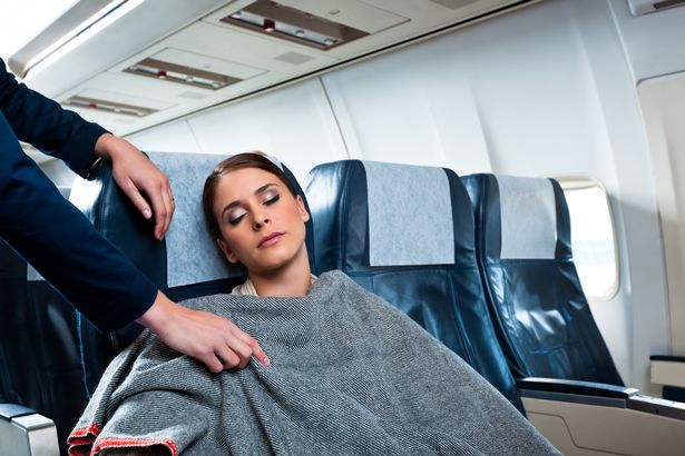 An air stewardess covering sleeping woman with a blanket 