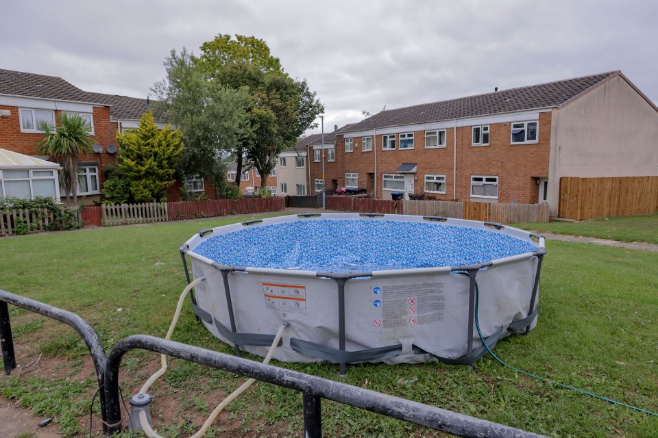 A round inflatable pool sits on a grassy area between houses.