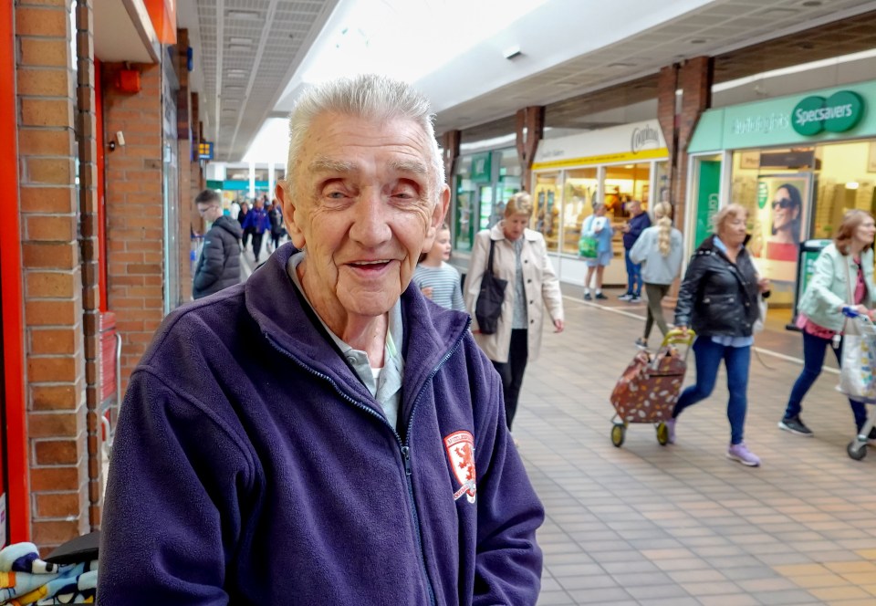 Smiling elderly man in a purple jacket in a shopping center.
