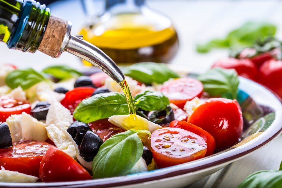 Olive oil being poured over a Caprese salad.