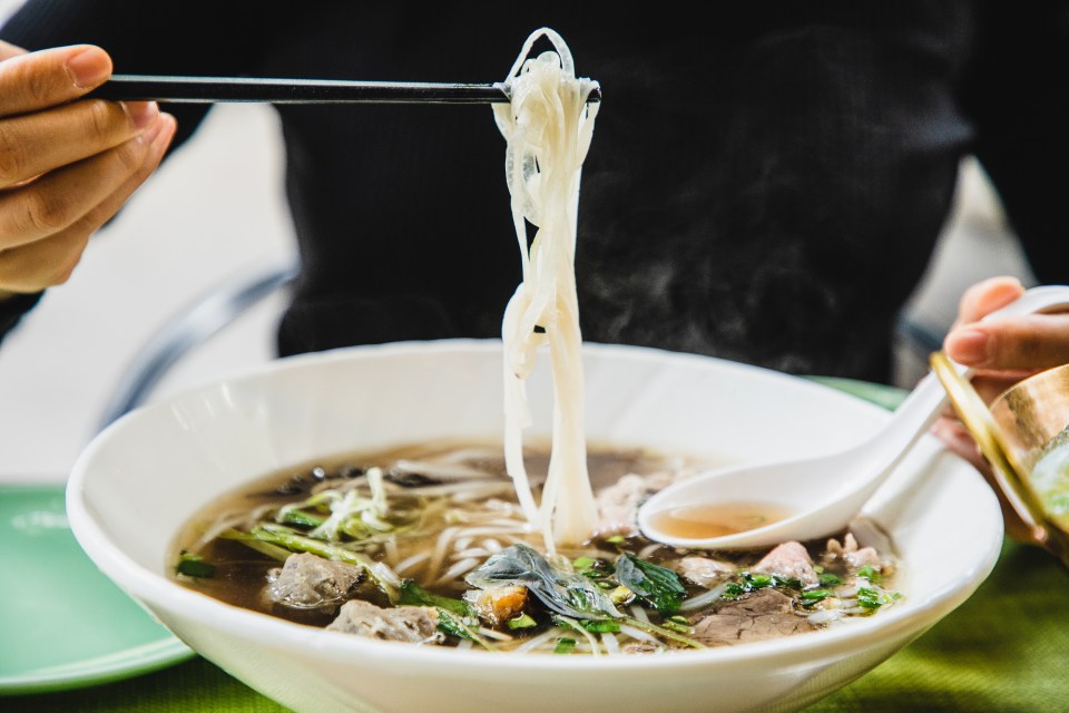 Person using chopsticks to eat a bowl of steaming pho.