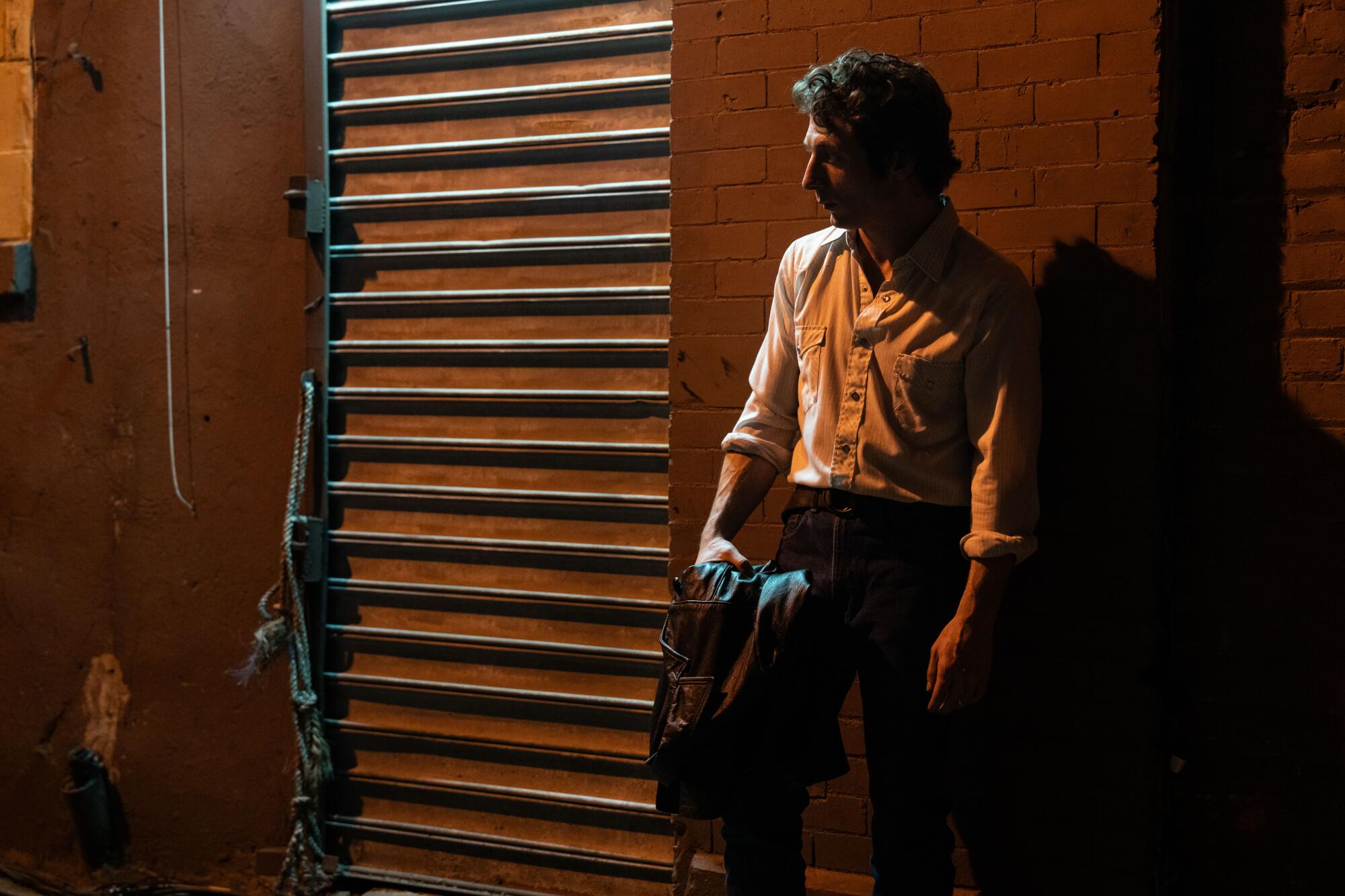 A man in shadows stands in front of a brick wall.