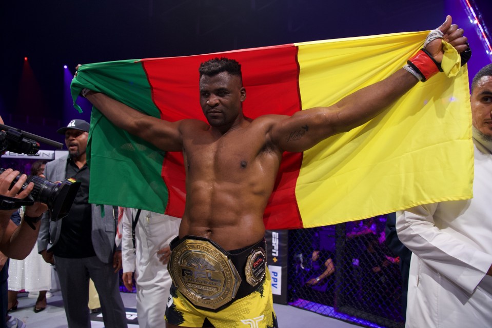 Francis Ngannou of Cameroon holding the PFL Heavyweight World Championship belt and the Cameroonian flag after a victory.
