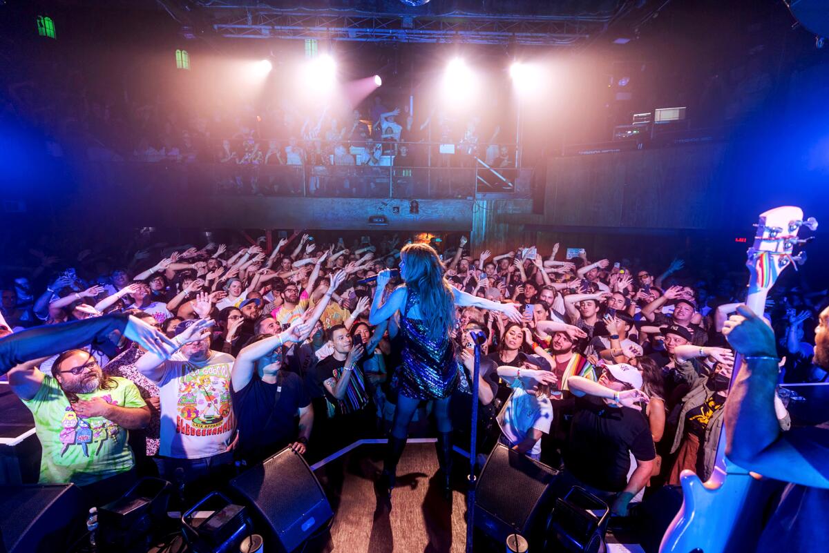 Carly Rae Jepsen sings on stage in front of audience members with arms outstretched.