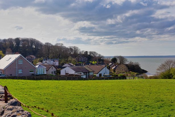 A scenic view of houses near a body of water under a cloudy sky, with a green field in the foreground in Heysham - Lancaster district - Lancashire - Great Britain