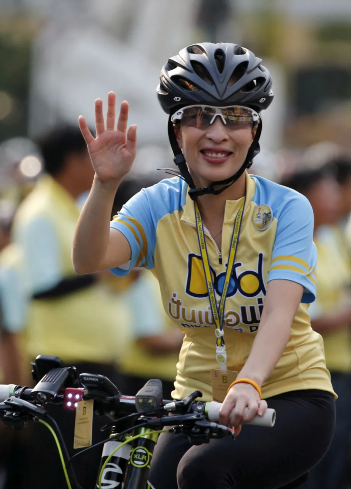 Woman in cycling helmet waving while on bicycle.