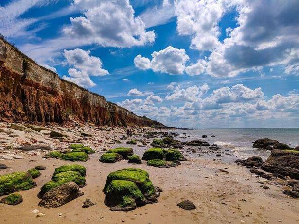 Scenic beach view of white and orange chalk and limestone cliffs at Old Hunstanton, Norfolk, England. Sand, sea, blue sky, white clouds and green rock