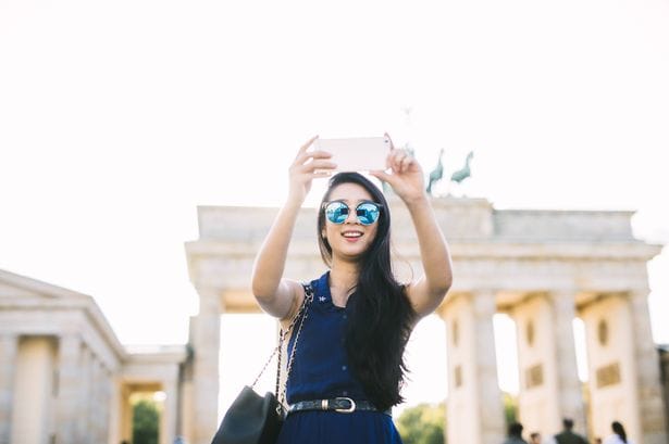 Young tourist woman taking a selfie with her smartphone at Brandenburg Gate.