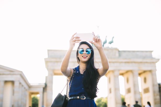 Young tourist woman taking a selfie with her smartphone at Brandenburg Gate.