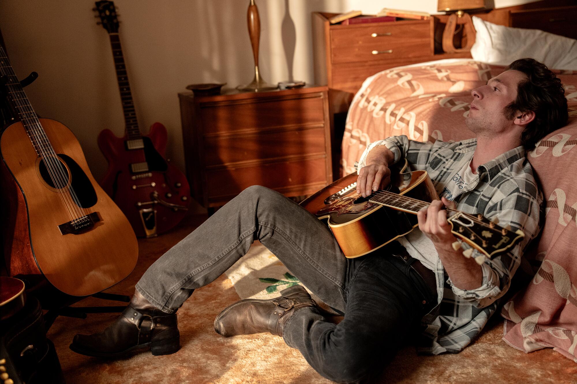 A man strums a guitar in a bedroom.