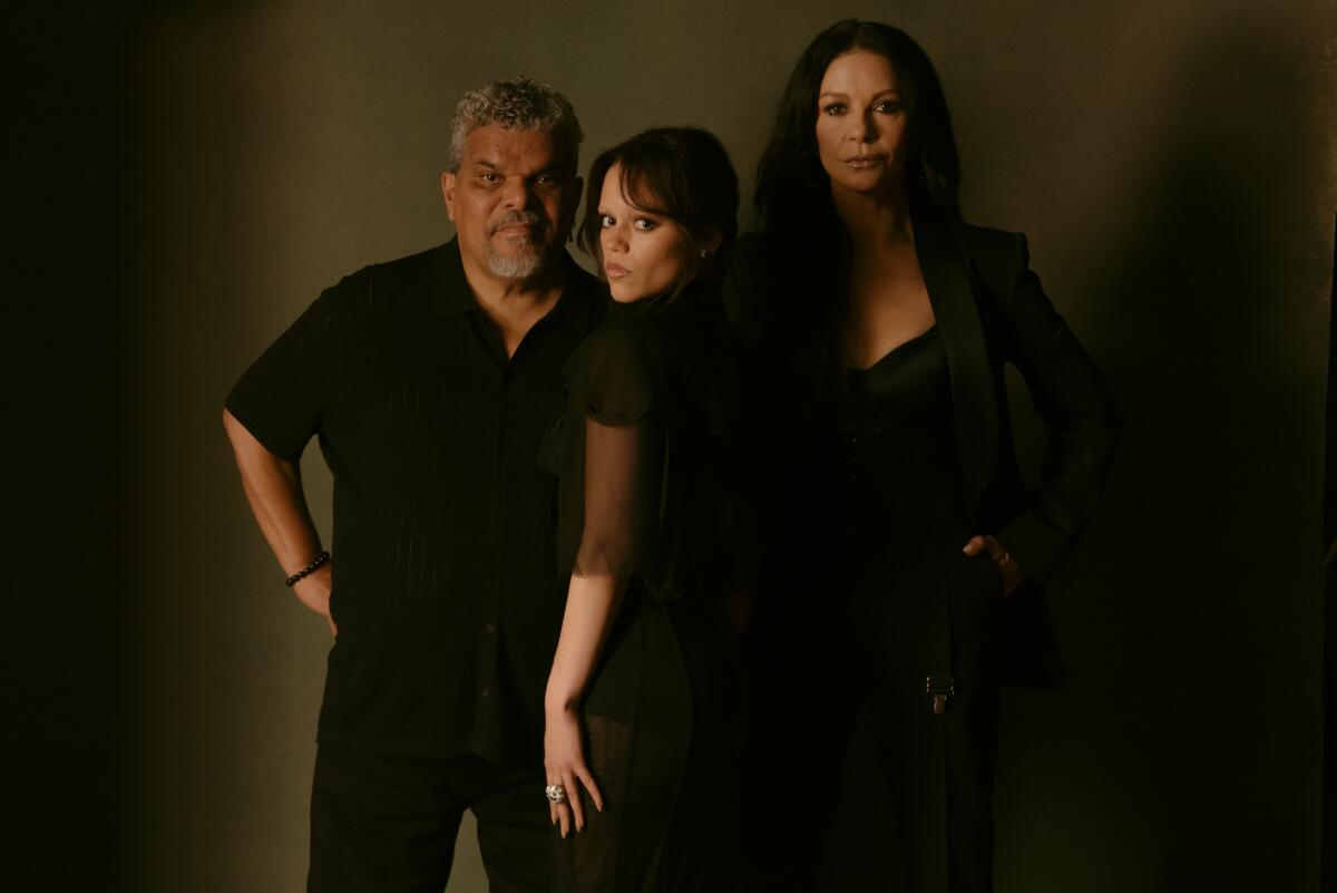 A man and a woman stand slightly behind a younger woman whose back is turned and is looking over her shoulder.