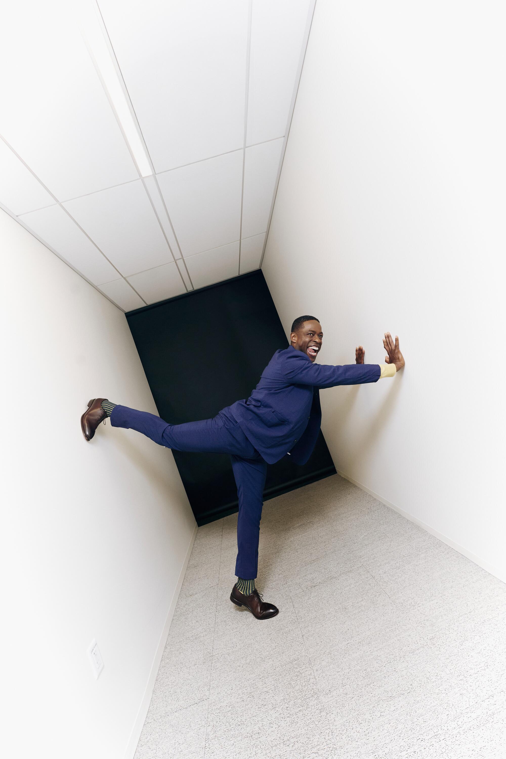 Sterling K. Brown in a blue suit in a blank hallway.