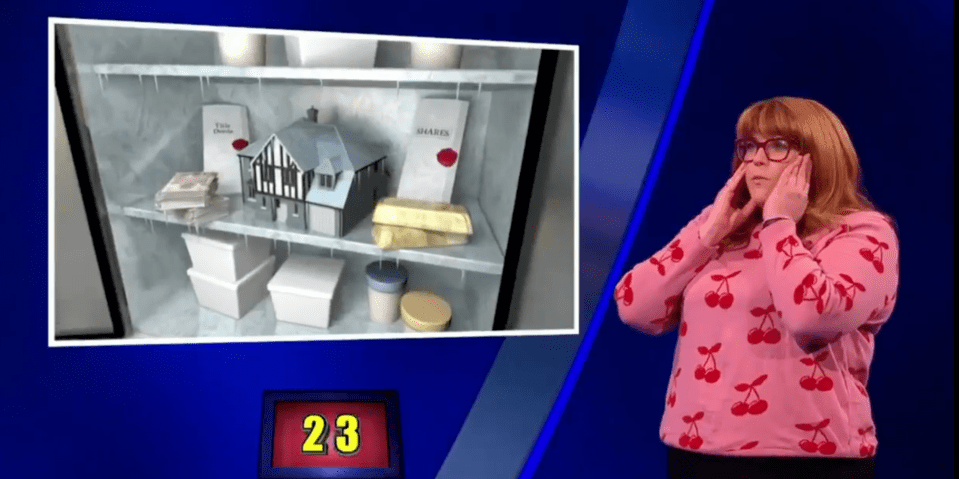 Screenshot of a game show contestant reacting to an image of a refrigerator containing cash, a house model, gold bars, and shares.  The number 23 is displayed.