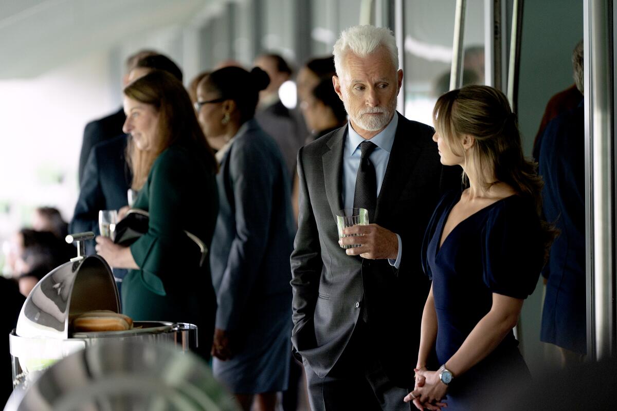 A man holding a glass looks down toward a woman in a blue dress at a reception.