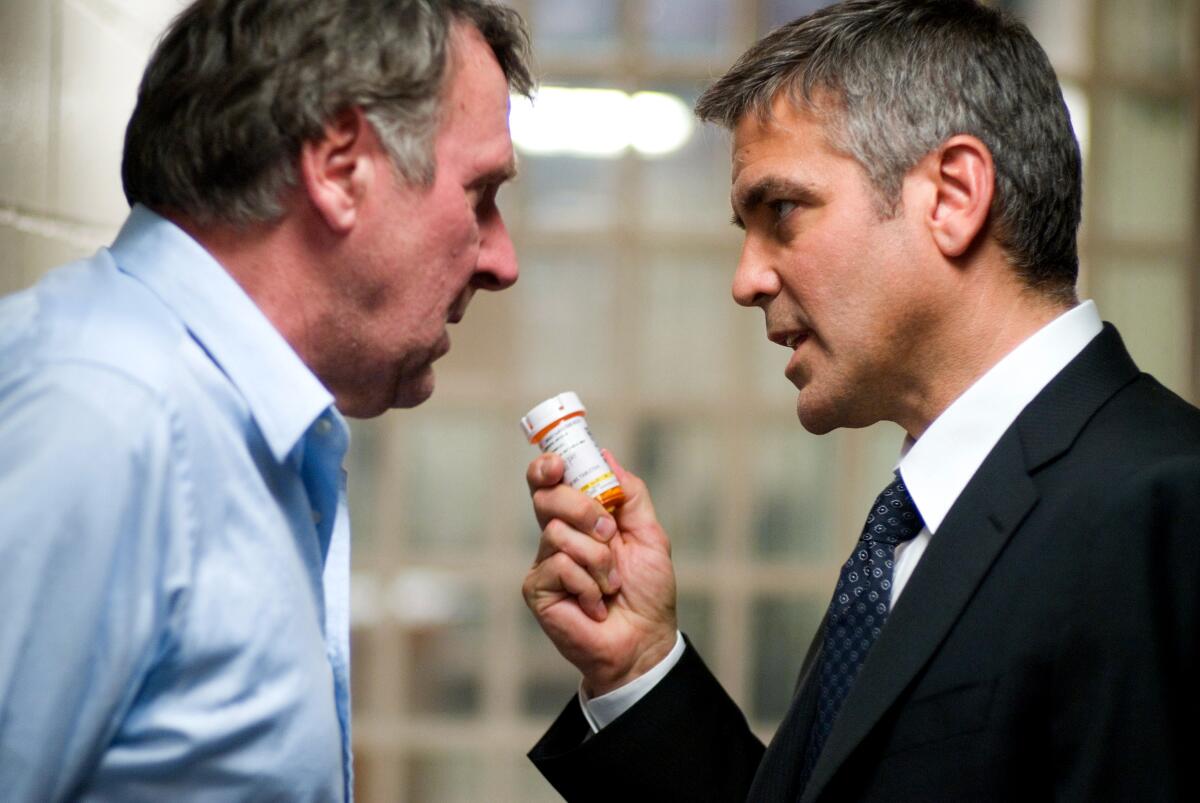 Two men, one holding a prescription bottle, talking.
