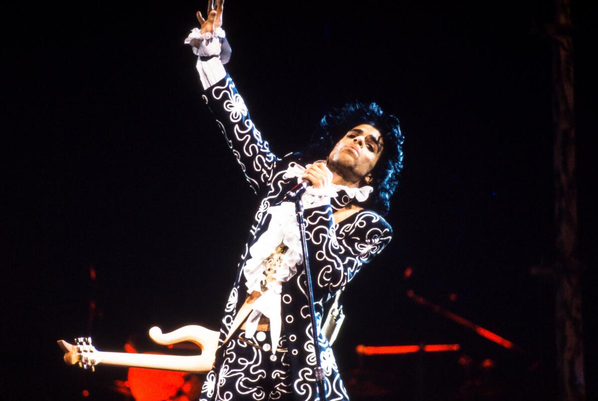 A musician holding a mic stand reaches skyward with his right hand.