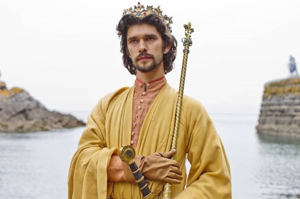 A man in yellow robes and a crown stands by the sea