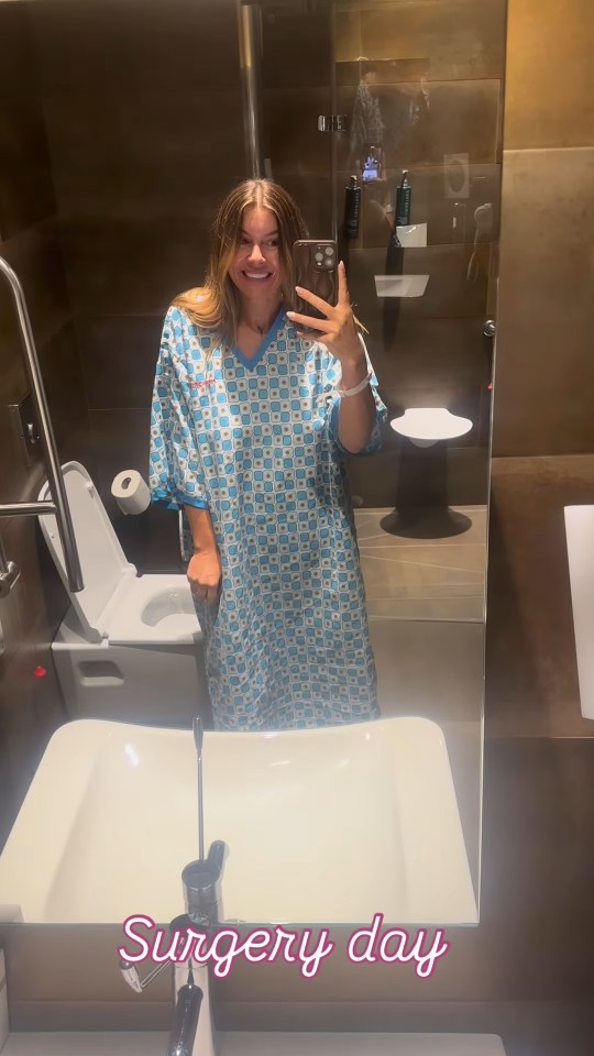 Woman in a hospital gown taking a selfie in a bathroom mirror on her surgery day.