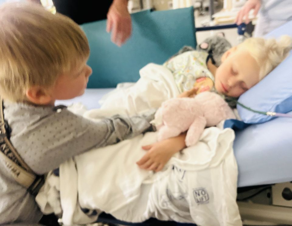 A young child visits their sibling in a hospital bed.