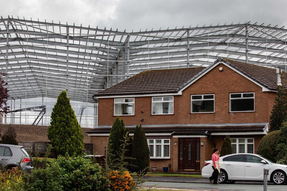 Large steel structure under construction overshadowing houses.