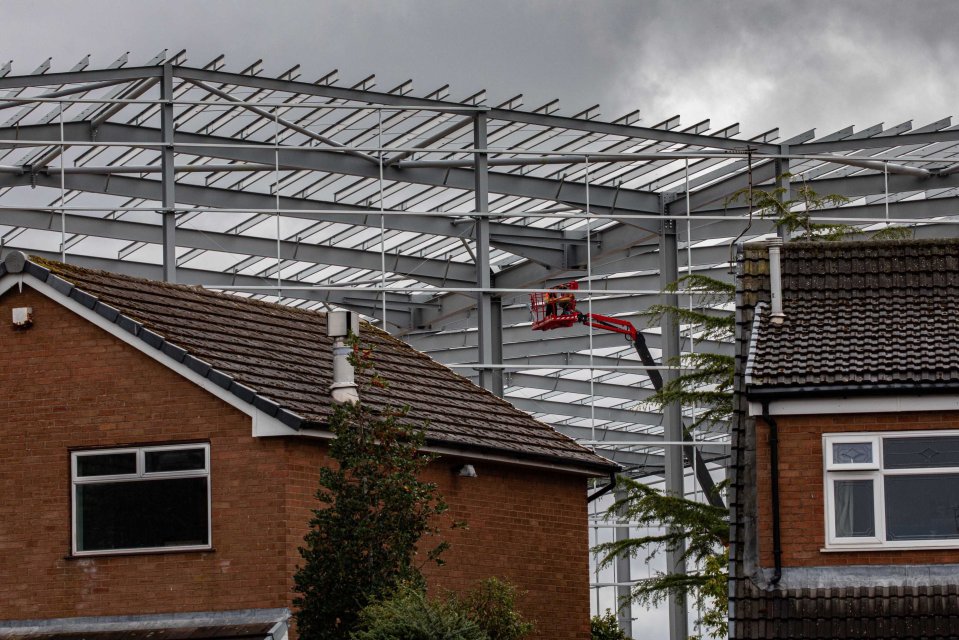 Large steel structure under construction looming over houses.