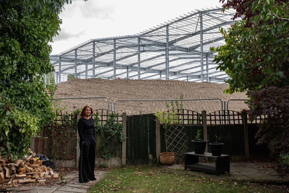 Woman stands in her garden next to a large warehouse under construction.