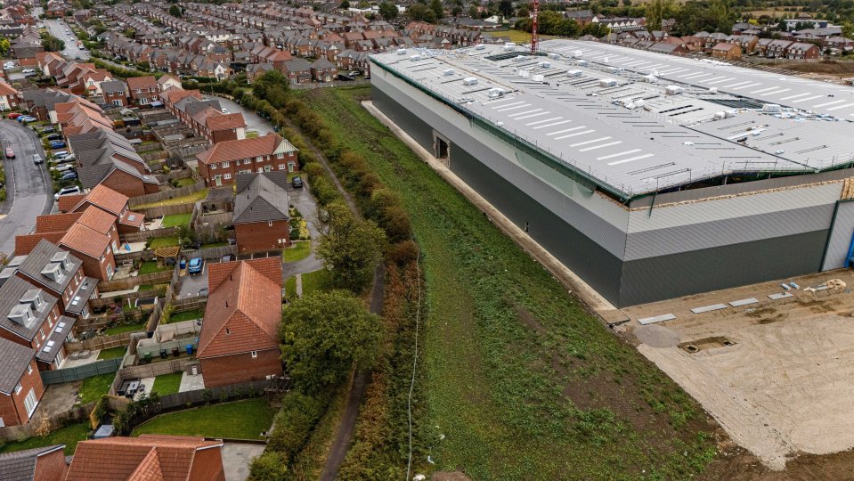 Woman looking at a large warehouse under construction from her back garden.