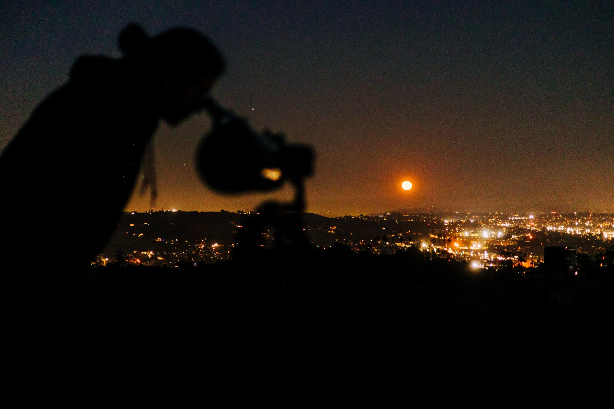 A person looks through a telescope at night.