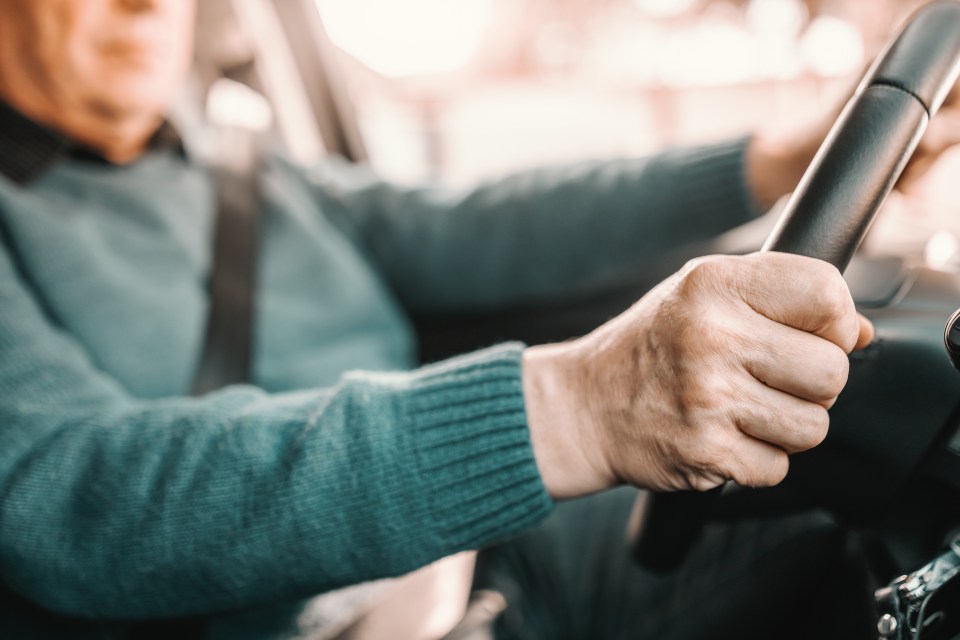 Close-up of a senior man's hands gripping a car's steering wheel.
