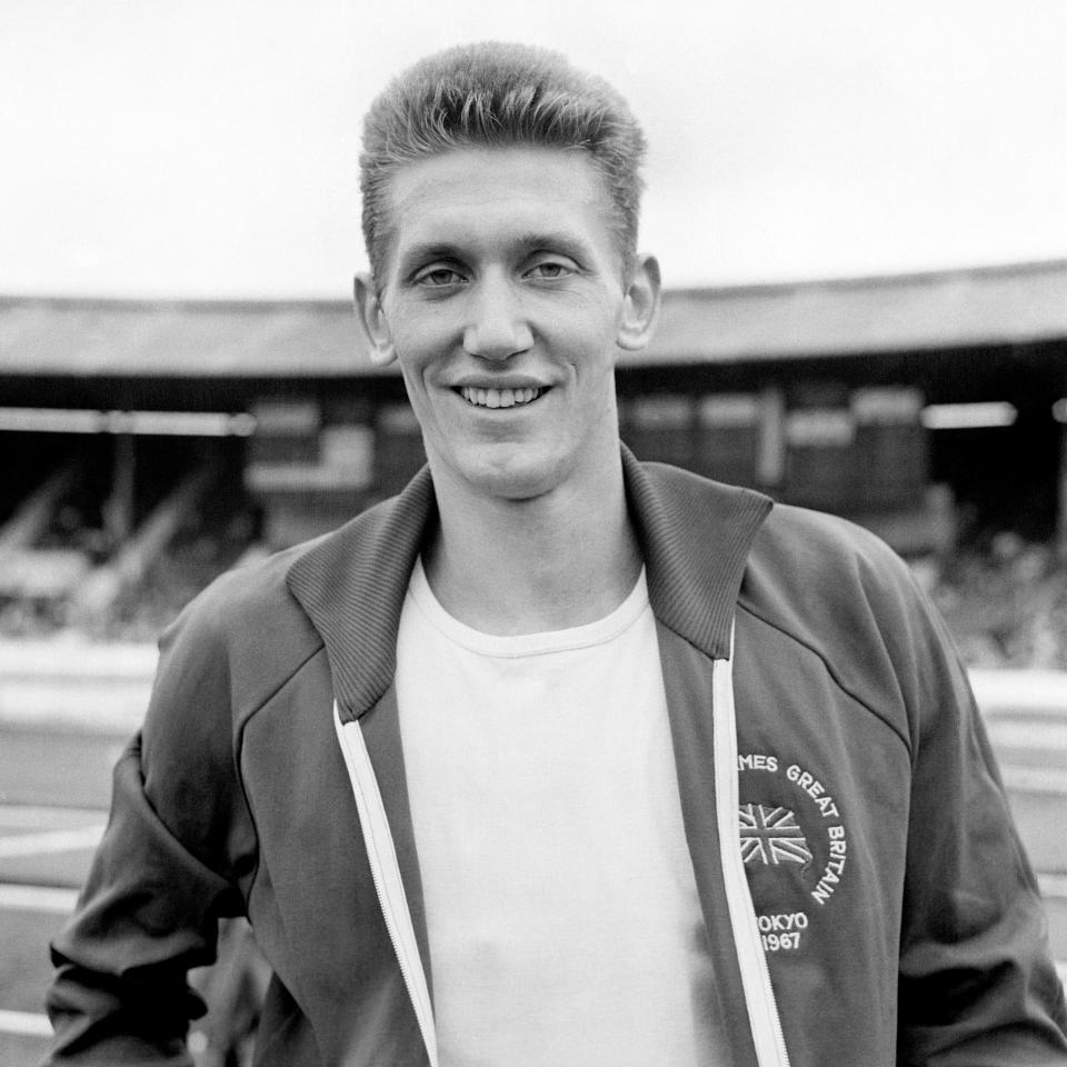 Black and white photo of a smiling man in a Great Britain Olympic jacket.
