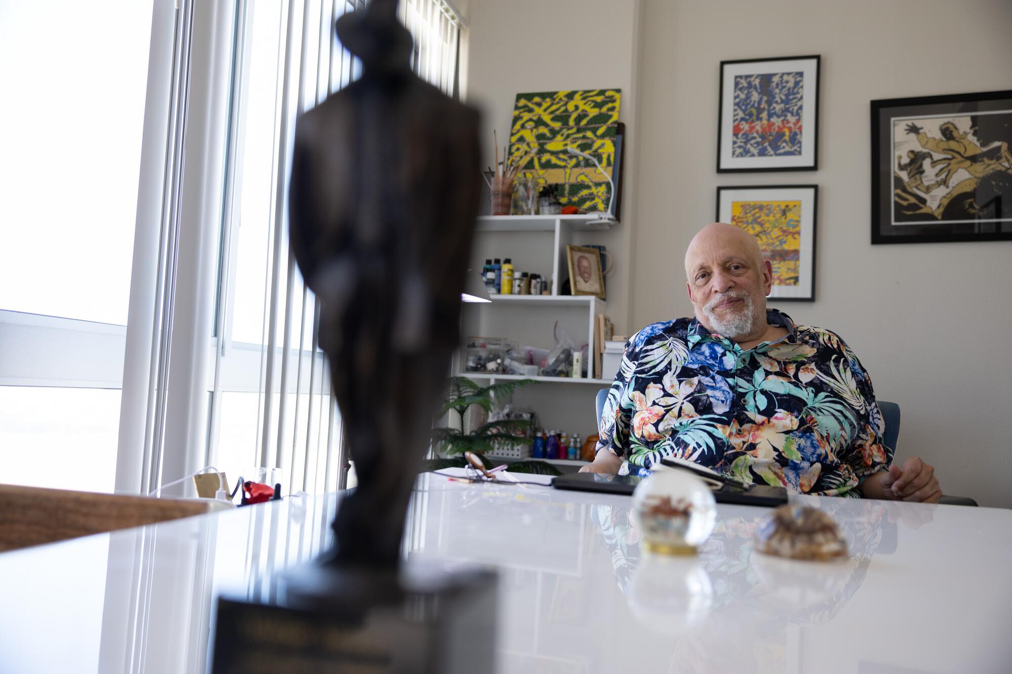 Walter Mosley sits behind a table, in front of a wall of art and a bookshelf.