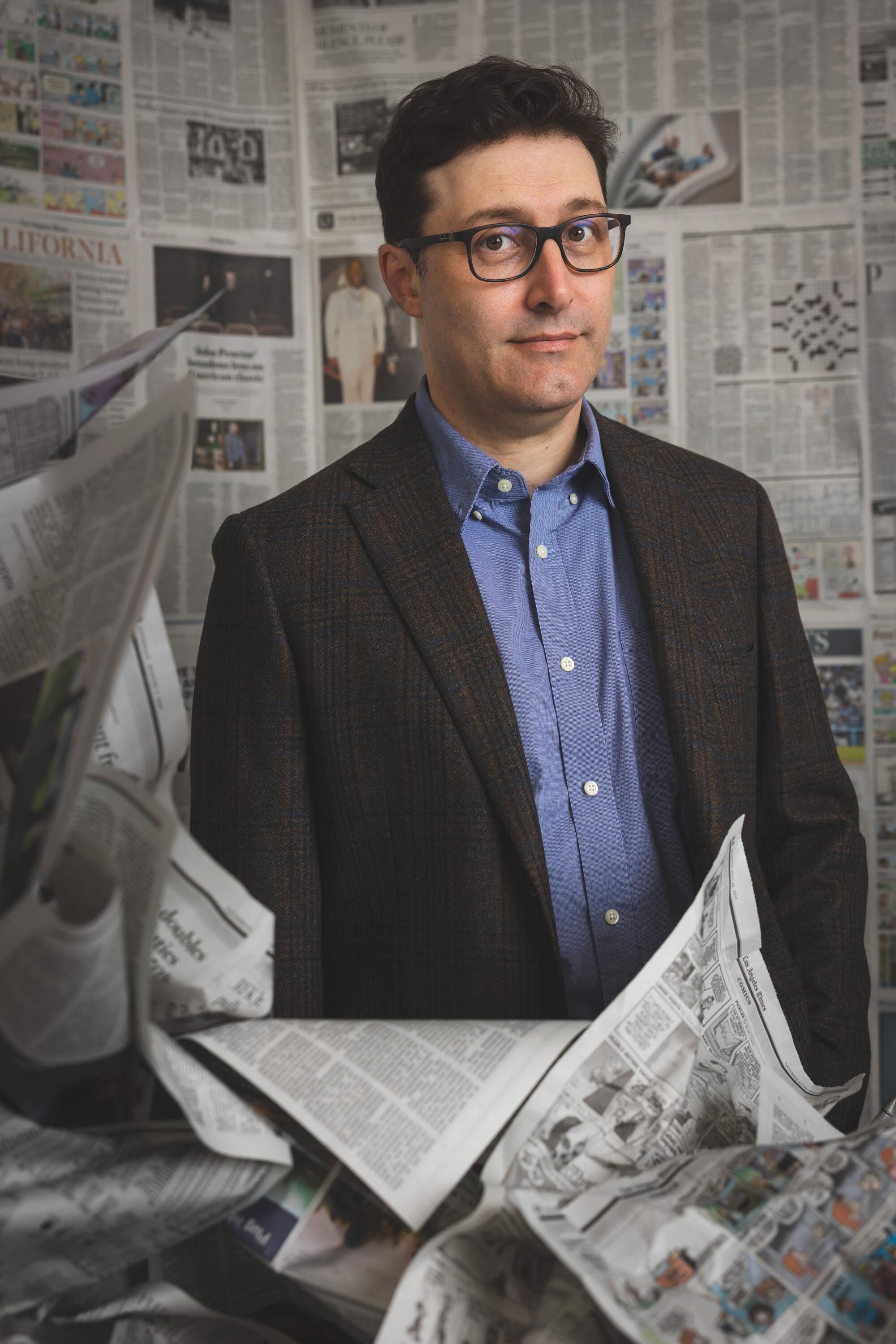 A man poses for a photo surrounded by newspapers