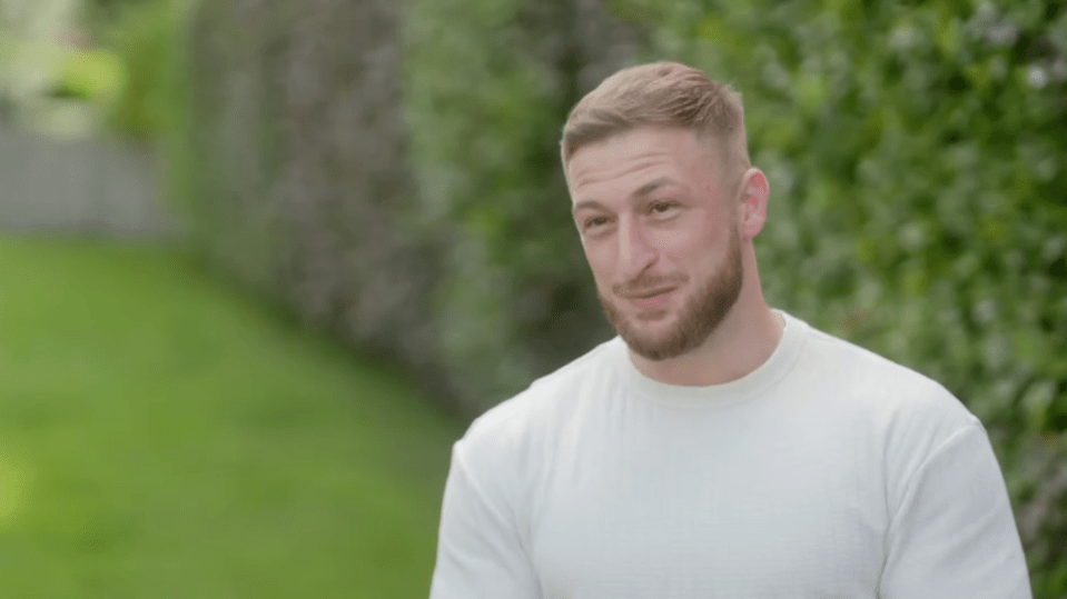 Man in a white shirt smiling outdoors.