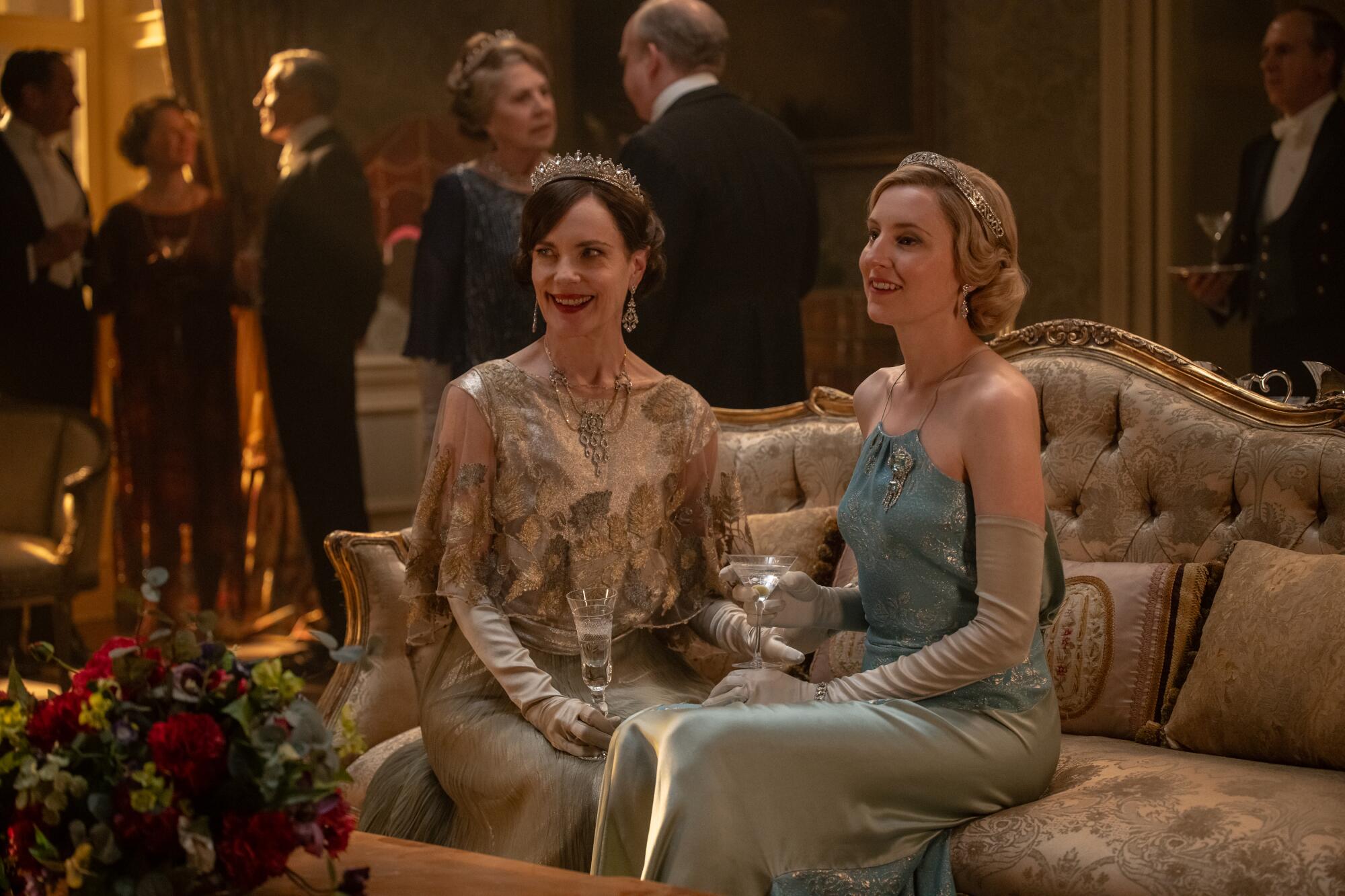 A woman in a blue sleeveless gown smiles at a cocktail gathering.