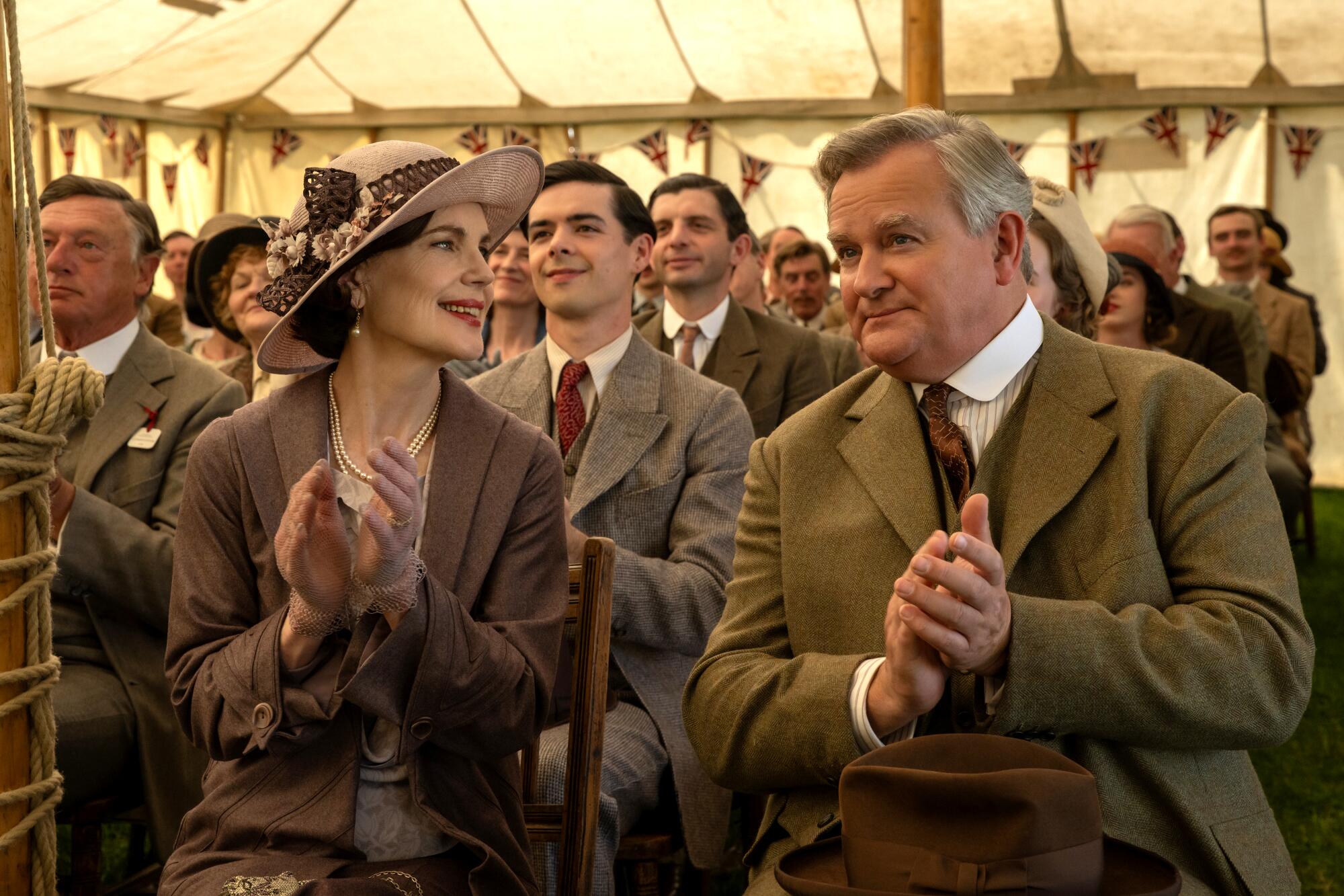 A man and his wife applaud at a tented gathering.