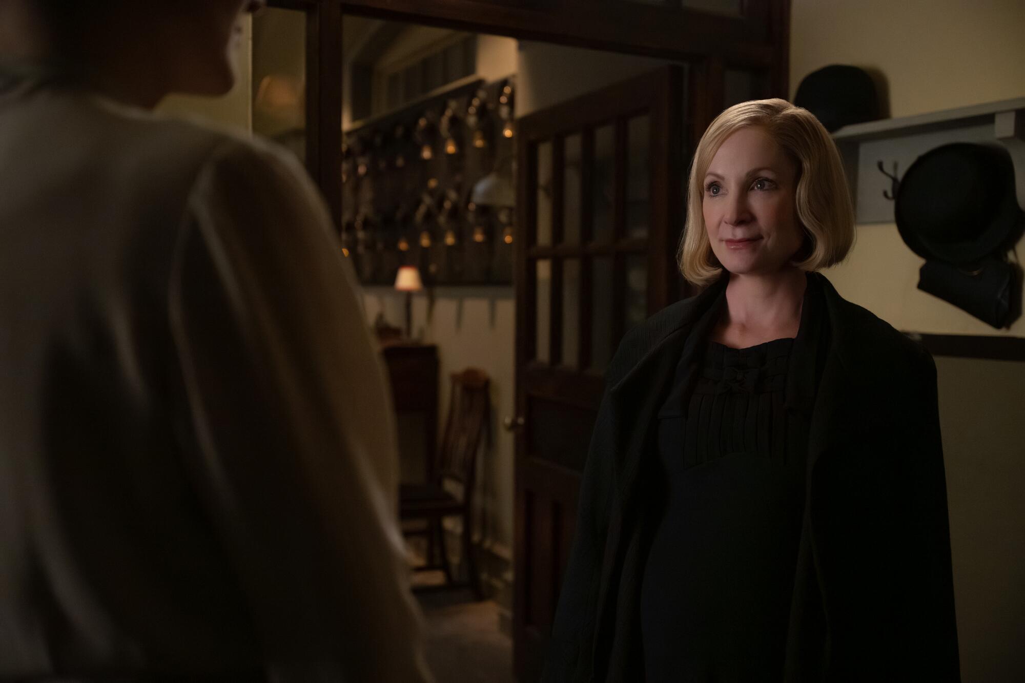 A woman in a dark coat speaks.